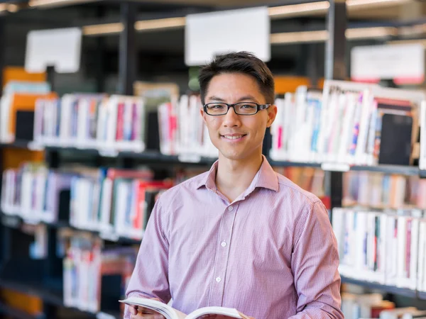 Glücklicher männlicher Student mit Büchern in der Bibliothek — Stockfoto