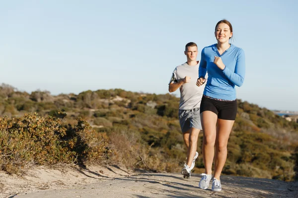 Sportlerin joggt mit ihrem Partner am Strand — Stockfoto