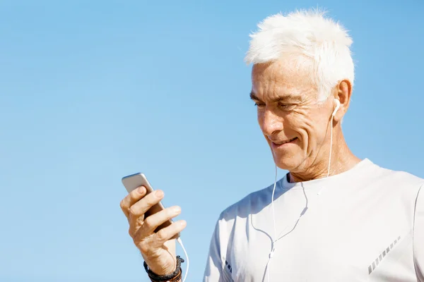 Male runner with his mobile smart phone standing outdoors — Stock Photo, Image