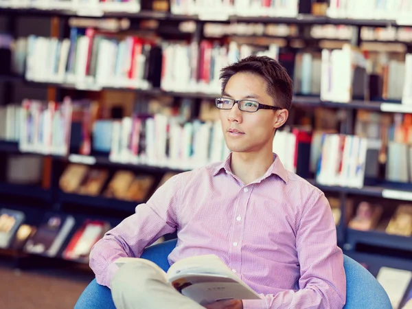 Estudante do sexo masculino feliz segurando livros na biblioteca — Fotografia de Stock