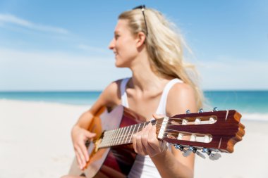 Güzel genç bir kadın sahilde gitar çalıyor.