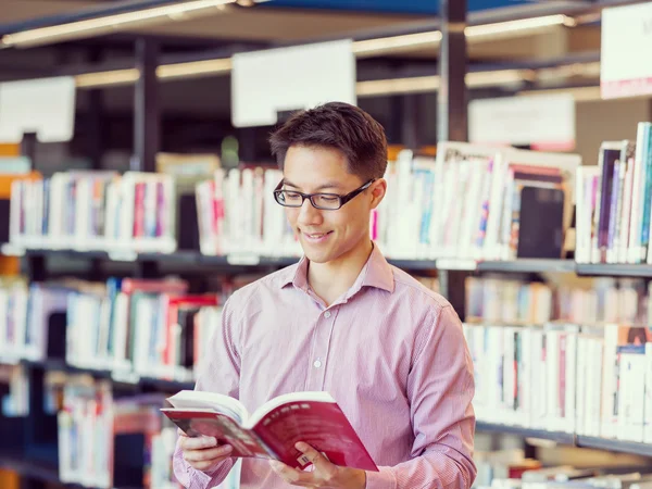 Estudante do sexo masculino feliz segurando livros na biblioteca — Fotografia de Stock