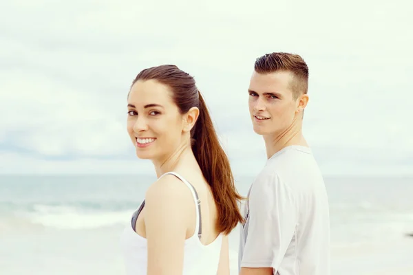 Ungt par tittar på kameran när du står bredvid varandra på stranden — Stockfoto