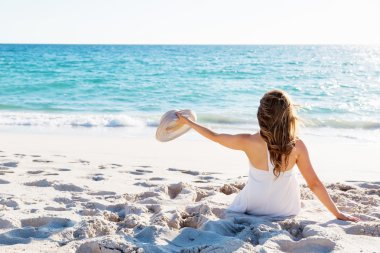 Genç bir kadın sahilde oturuyor.