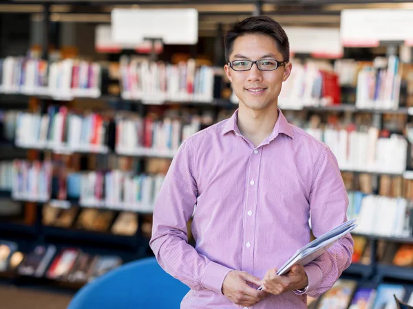 Glücklicher männlicher Student mit Büchern in der Bibliothek — Stockfoto