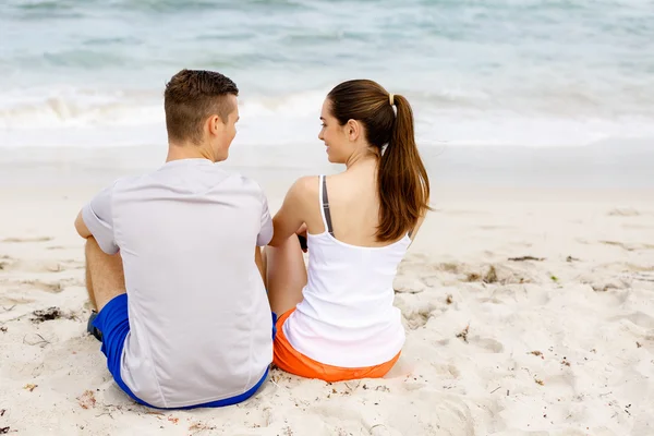 Casal jovem olhando um para o outro enquanto sentado na praia — Fotografia de Stock