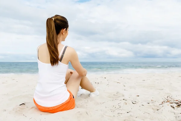 Mujer joven en ropa deportiva sentada en la playa — Foto de Stock