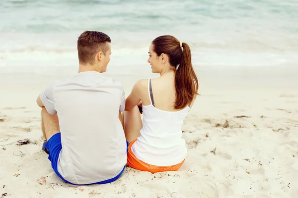 Casal jovem olhando um para o outro enquanto sentado na praia — Fotografia de Stock