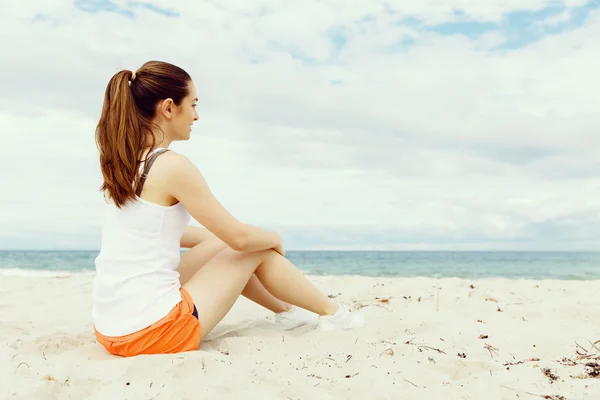 Jonge vrouw in sport slijtage zittend op het strand — Stockfoto