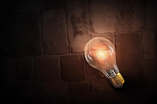 Glowing bulb on brick surface . Mixed media — Stock Photo, Image