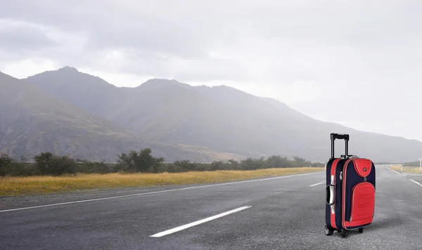 Red suitcase on road . Mixed media — Stock Photo, Image