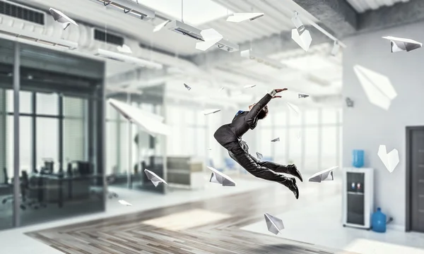 Jumping businessman in office . Mixed media — Stock Photo, Image