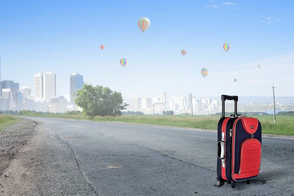 Red suitcase on road . Mixed media — Stock Photo, Image