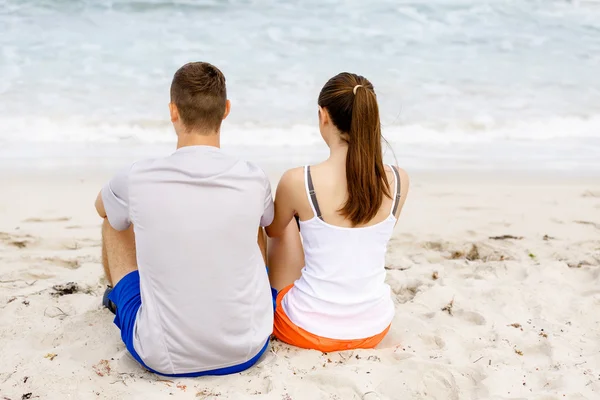 Casal jovem olhando um para o outro enquanto sentado na praia — Fotografia de Stock