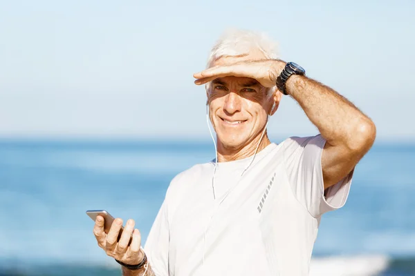 屋外に立っている彼の携帯のスマート フォンで男性ランナー — ストック写真