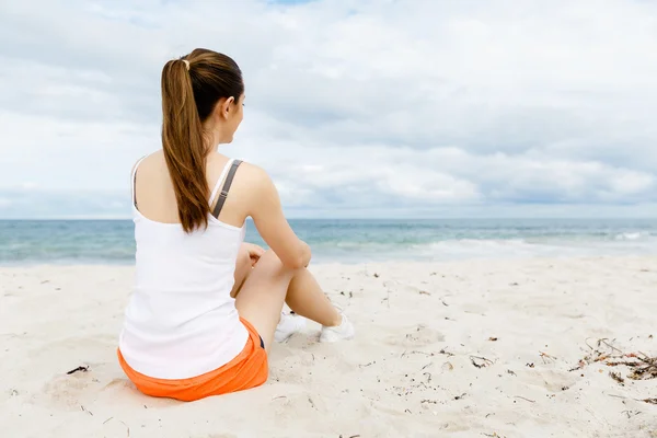 Jonge vrouw in sport slijtage zittend op het strand — Stockfoto