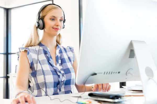 Jovem mulher ouvindo a música enquanto trabalhava em um computador — Fotografia de Stock