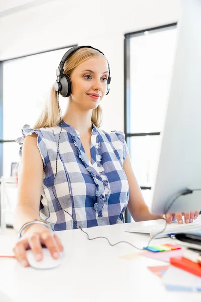 Junge Frau hört Musik, während sie am Computer arbeitet — Stockfoto