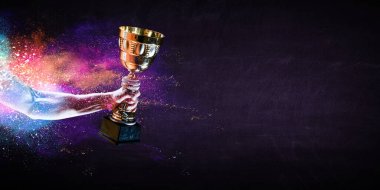 Hand holding up a gold trophy cup against dark background clipart
