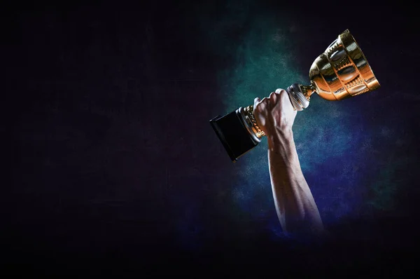 Hand holding up a gold trophy cup against dark background — Stock Photo, Image