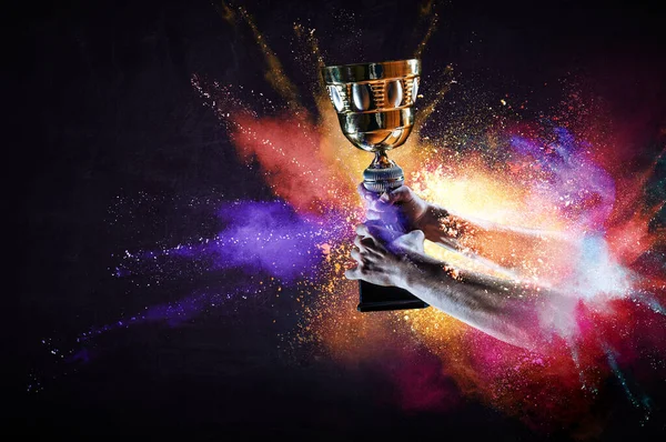 Hand holding up a gold trophy cup against dark background — Stock Photo, Image