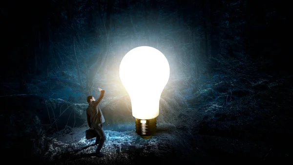 Huge light bulb glowing in the darkness . Mixed media — Stock Photo, Image