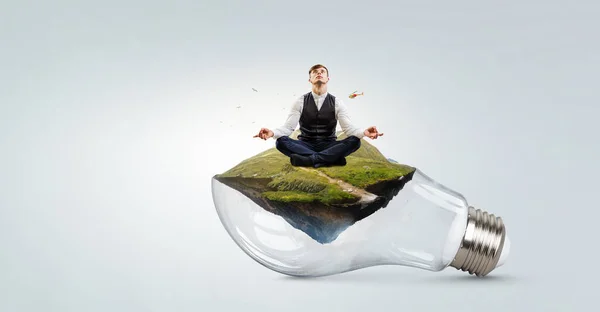Geschäftsmann beim Yoga in Lotus-Pose auf Glühbirne. Gemischte Medien — Stockfoto