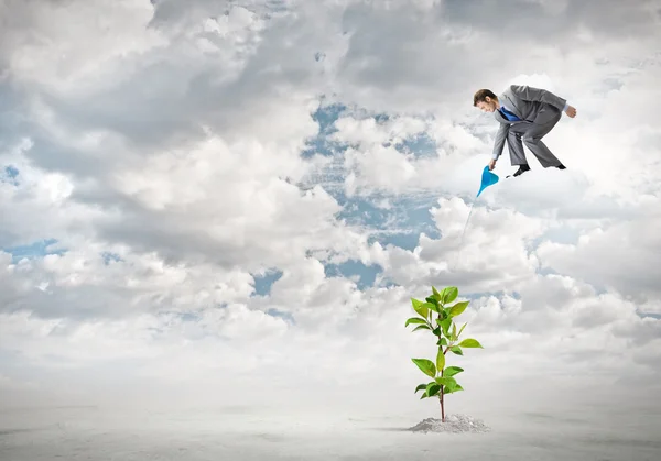 Businessman standing on cloud and watering sprout — Stock Photo, Image