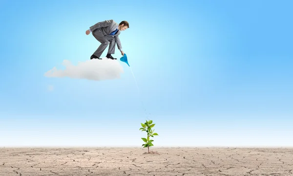 Businessman standing on cloud and watering sprout — Stock Photo, Image