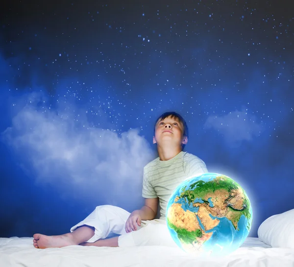 Junge sitzt im Bett und hält den Planeten Erde — Stockfoto