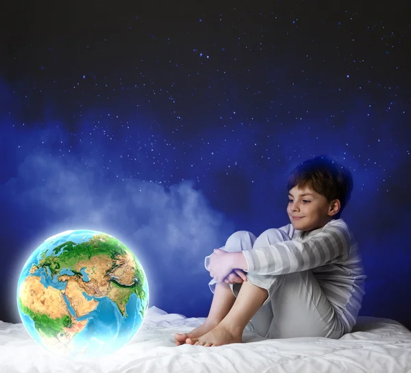 Niño sentado en la cama y mirando al planeta Tierra — Foto de Stock