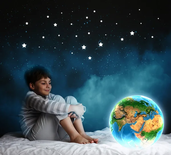 Jongen zitten in bed en kijken naar de planeet aarde — Stockfoto