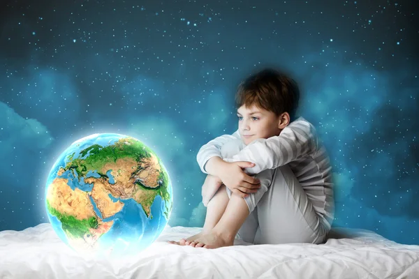 Мальчик сидит в постели и смотрит на планету Земля — стоковое фото