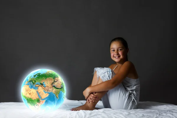 Meisje zitten in bed en kijken naar de planeet aarde — Stockfoto