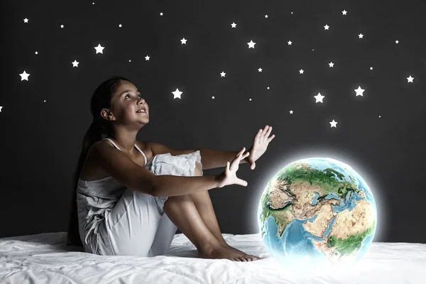 Девушка сидит в постели и смотрит на планету Земля — стоковое фото