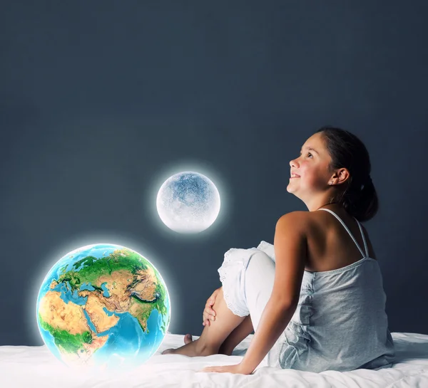 Girl sitting in bed and looking at Earth planet — Stock Photo, Image