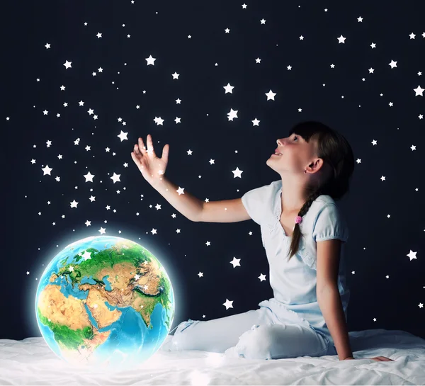 Mädchen sitzt im Bett und schaut auf den Planeten Erde — Stockfoto