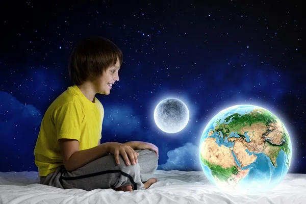 Chłopiec siedzi na łóżku trzymając planety ziemi — Zdjęcie stockowe