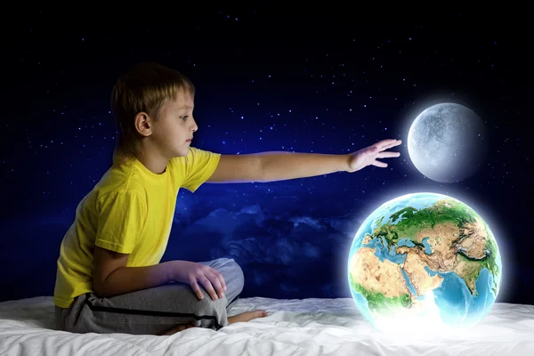 Pojken sitter i sängen håller jorden planet — Stockfoto