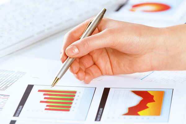 Hand holding pen and pointing at graphs