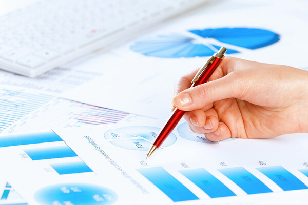 Hand holding pen and pointing at graphs