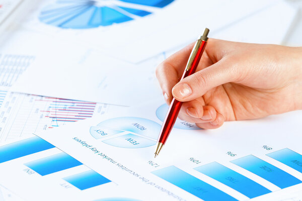 Hand holding pen and pointing at graphs