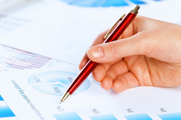 Hand holding pen and pointing at graphs