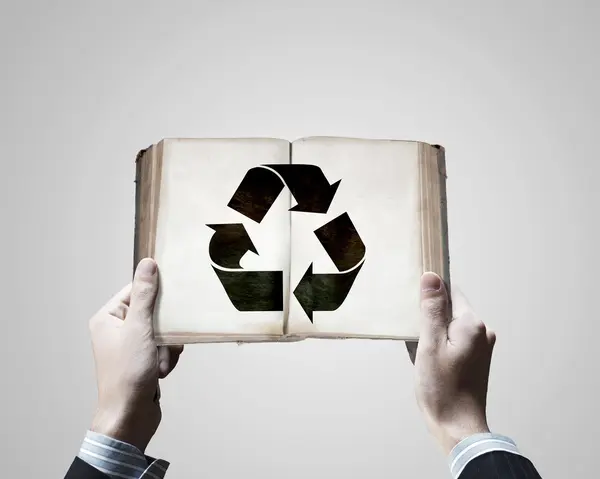 Manos sosteniendo libro con signo de reciclaje — Foto de Stock