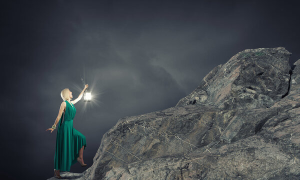 Young attractive woman in green dress with lantern walking in darkness