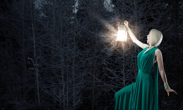 Young woman in green dress with lantern in darkness