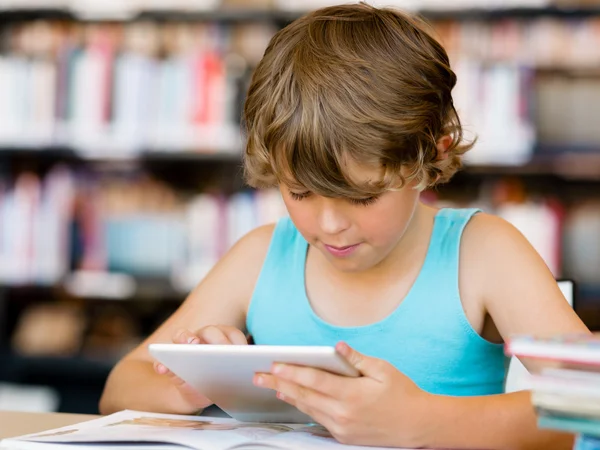 Menino da escola primária com tablet na biblioteca — Fotografia de Stock