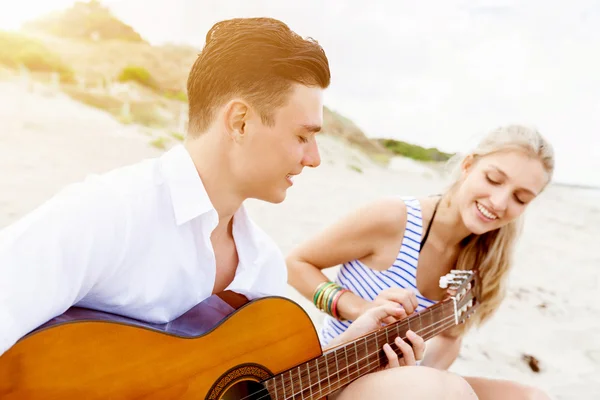 Pareja joven tocando la guitarra en la playa enamorada —  Fotos de Stock