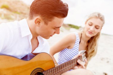 Genç çift aşık sahilde gitar çalmak