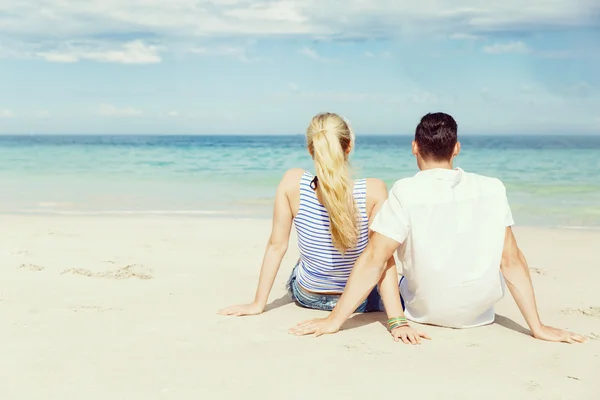 Romantische jonge paar zittend op het strand — Stockfoto